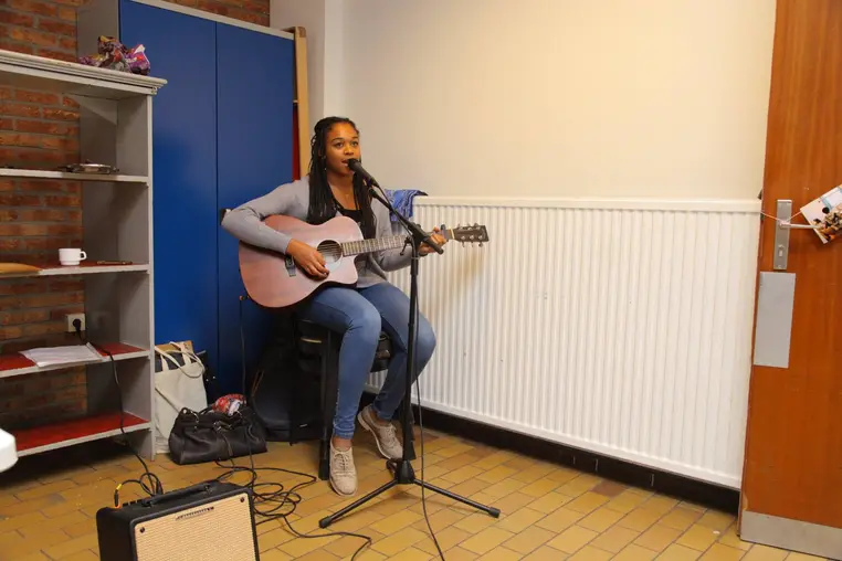 Une jeune femme chante au micro en s'accompagnant à la guitare.