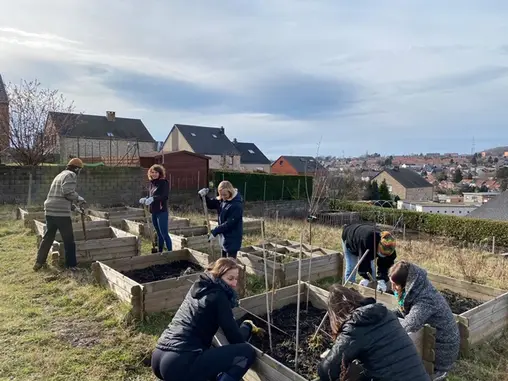 Un groupe bêche et plante dans des bacs potagers surélevés, en surplomb des toits du quartier.