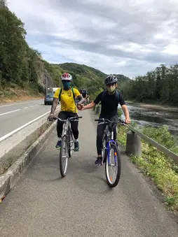 Deux cyclistes casqués roulent sur une piste cyclable le long de la Meuse.